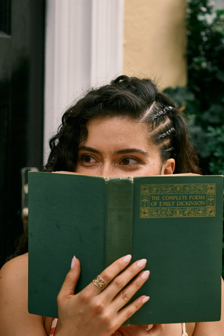 A woman peeking over a green copy of The Complete Poems of Emily Dickinson.